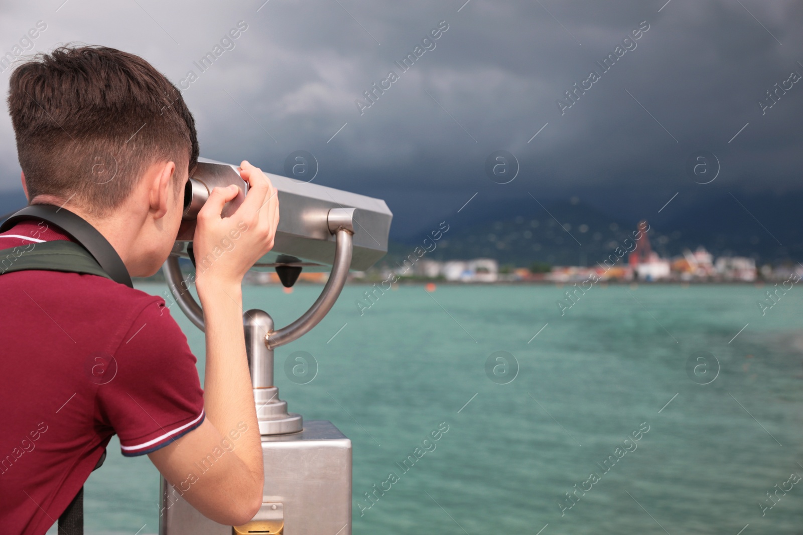 Photo of Teenage boy looking through mounted binoculars at mountains. Space for text