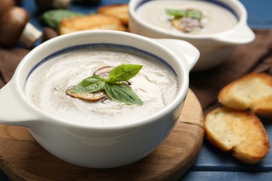 Photo of Fresh homemade mushroom soup ceramic pots on blue wooden table, closeup