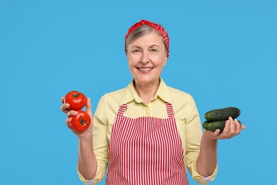 Photo of Happy housewife with tomatoes and cucumbers on light blue background