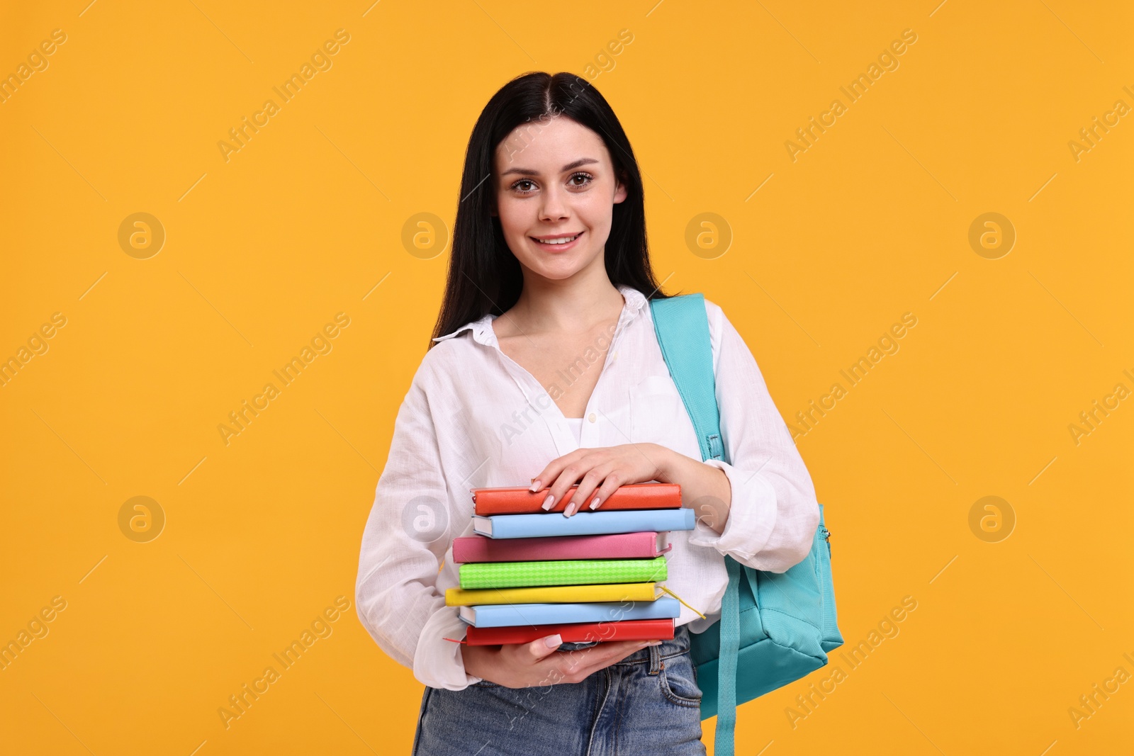 Photo of Smiling student with stack of books on yellow background