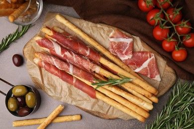 Photo of Delicious grissini sticks with prosciutto and snacks on brown table, flat lay