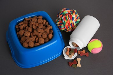 Bottle with vitamins, toys and dry pet food in bowl on grey background, above view