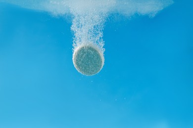 Effervescent pill dissolving in water on light blue background, closeup