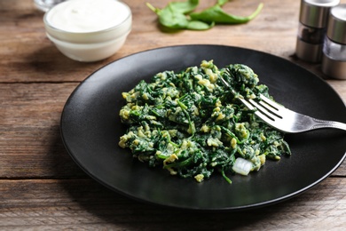 Photo of Tasty cooked spinach and fork on wooden table, closeup. Healthy food