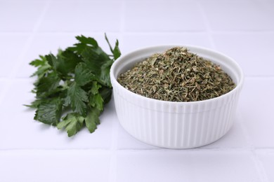 Photo of Dried parsley and fresh leaves on white tiled table, closeup