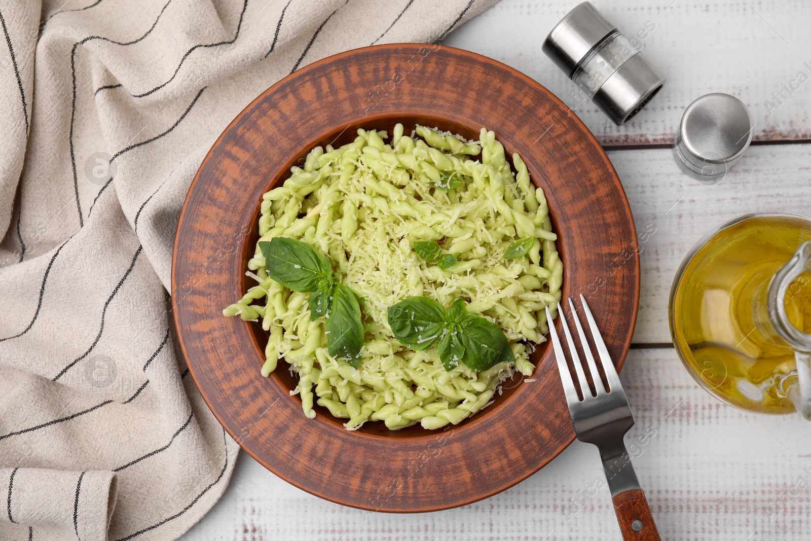 Photo of Plate of delicious trofie pasta with cheese and basil leaves on white wooden table, flat lay