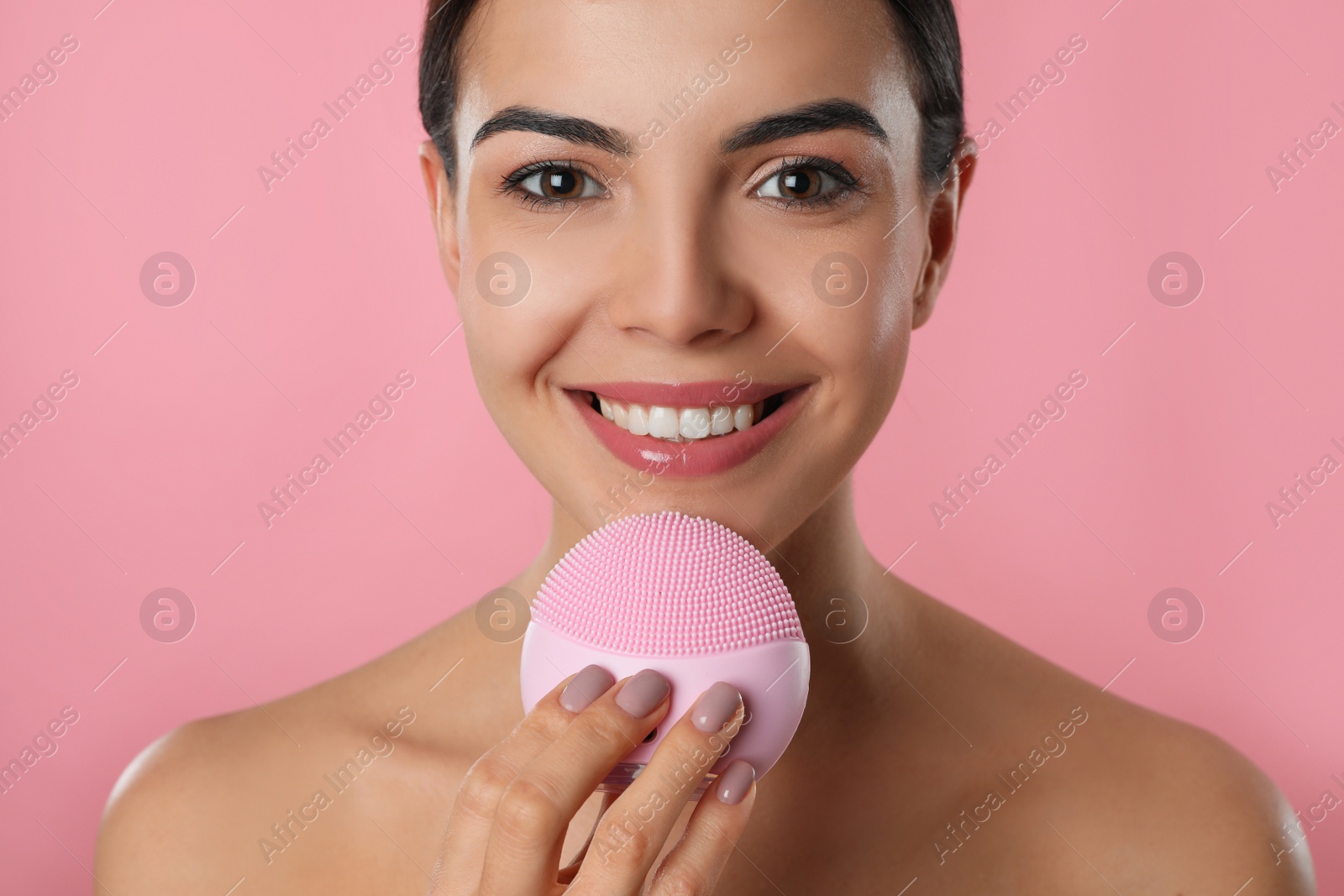 Photo of Young woman using facial cleansing brush on pink background, closeup. Washing accessory