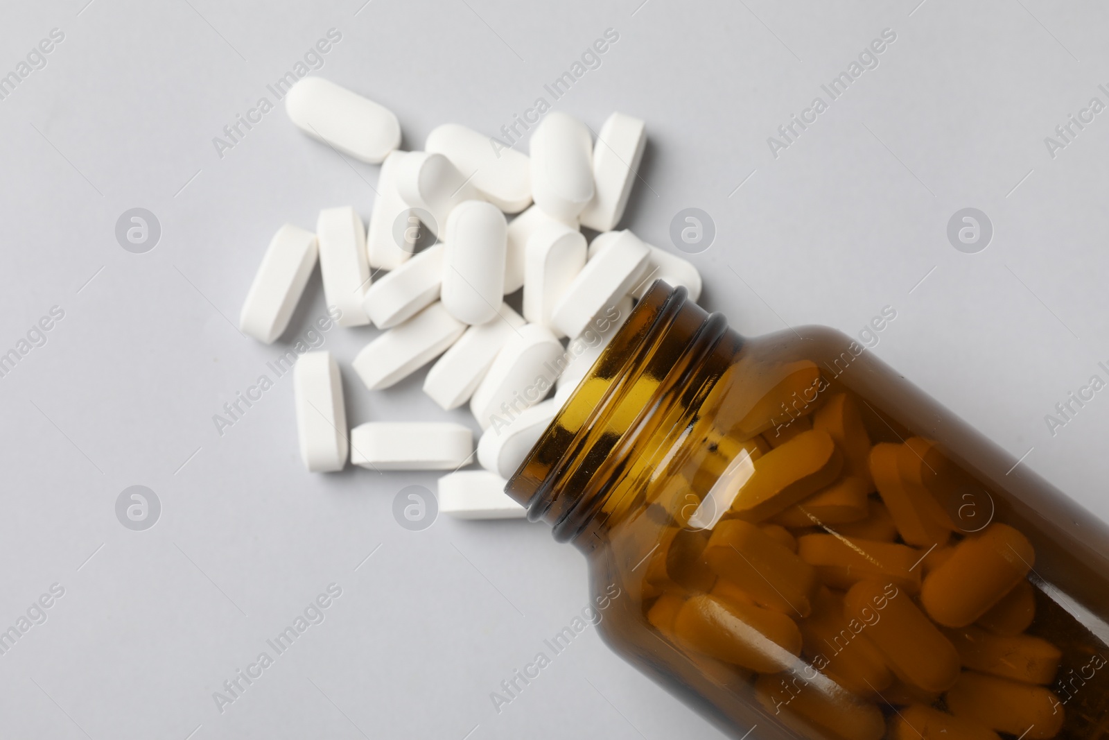 Photo of Vitamin pills and bottle on light grey background, top view