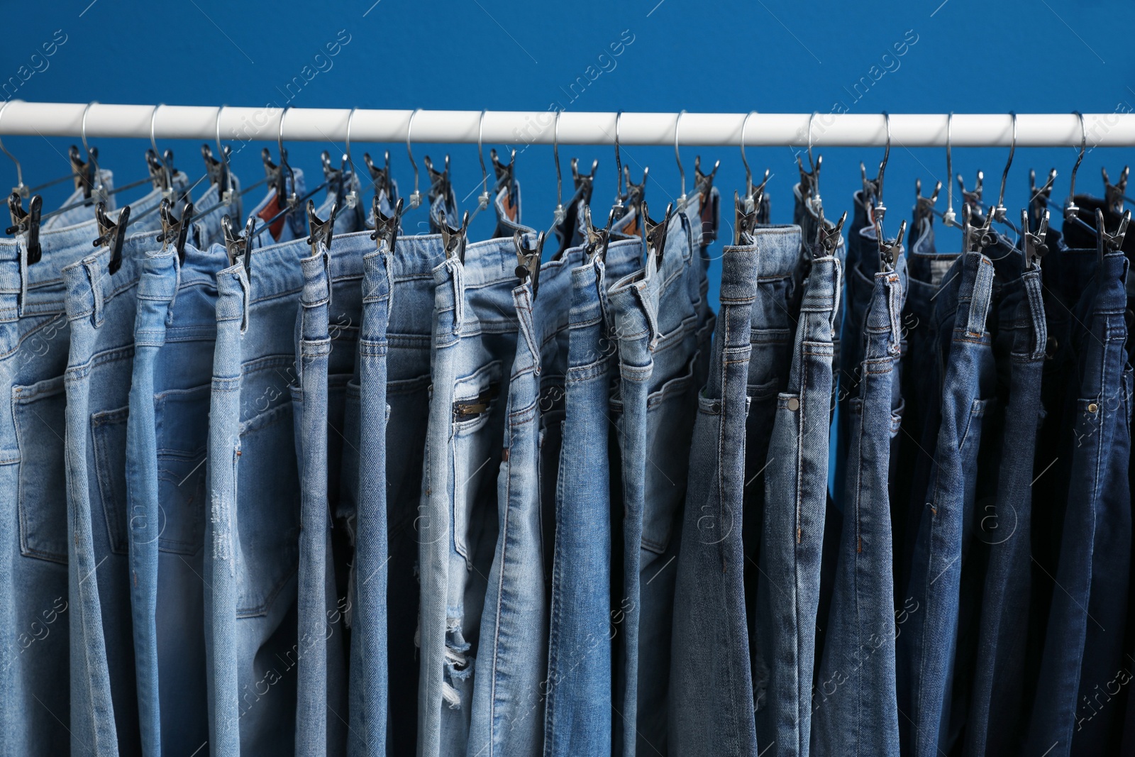 Photo of Rack with stylish jeans on blue background, closeup