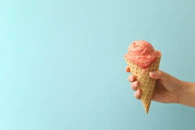Photo of Woman holding waffle cone with delicious pink ice cream on light blue background, closeup. Space for text