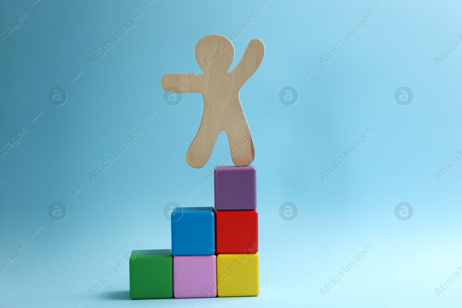 Photo of Wooden human figure on top of block staircase against light blue background. Career promotion concept