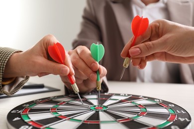 Business targeting concept. People with darts aiming at dartboard at table, closeup