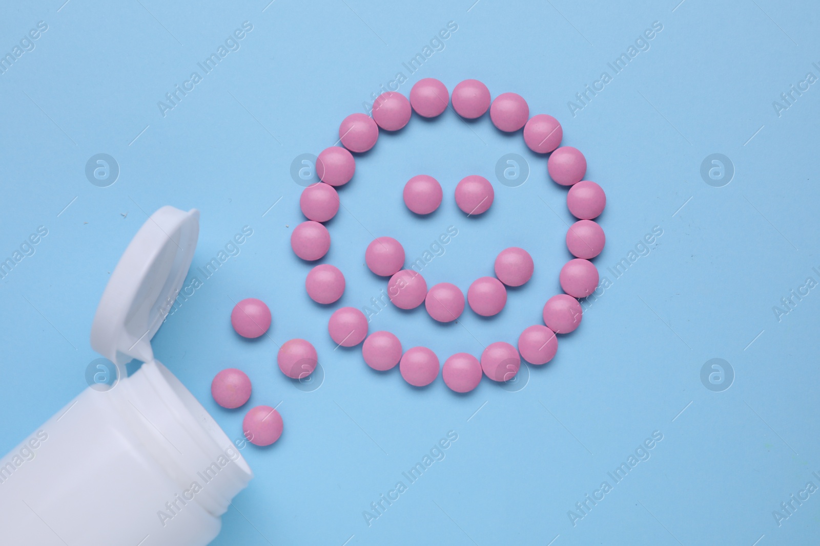 Photo of Happy face made of antidepressant pills and bottle on light blue background, flat lay