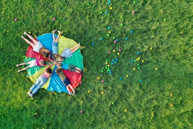 Photo of Group of children with teachers holding hands together on rainbow playground parachute in park, top view. Summer camp activity