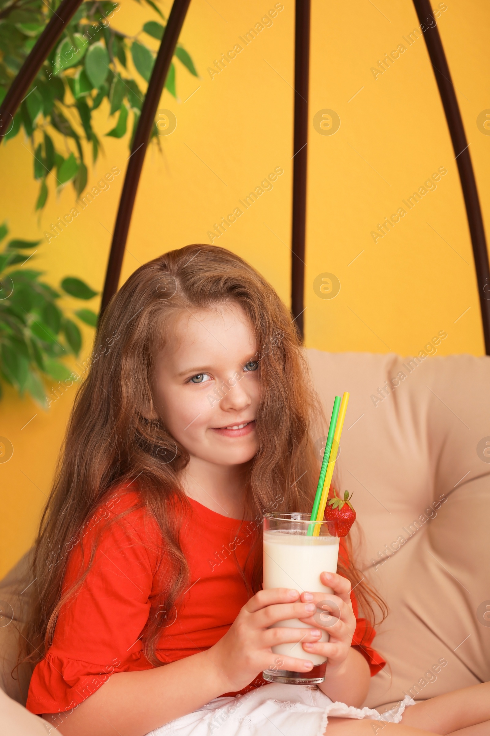 Photo of Little girl with glass of delicious milk shake in pendant chair indoors