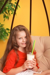 Little girl with glass of delicious milk shake in pendant chair indoors