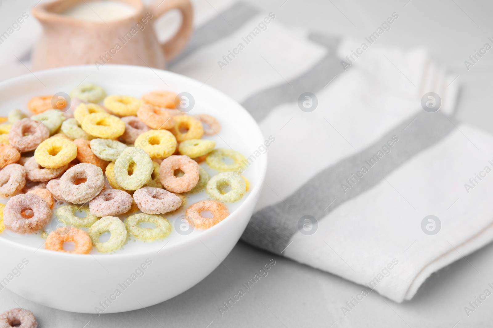 Photo of Cereal rings and milk in bowl on white table, closeup. Space for text