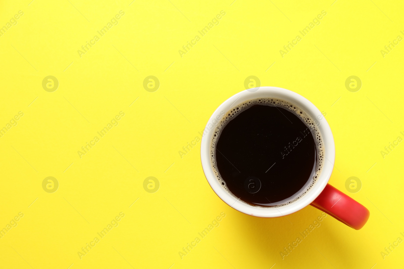 Photo of Aromatic coffee in cup on yellow background, top view. Space for text