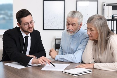 Photo of Insurance agent consulting elderly couple about pension plan at wooden table in office