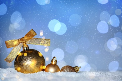 Image of Beautiful golden Christmas balls on snow against blurred festive lights, bokeh effect. Space for text