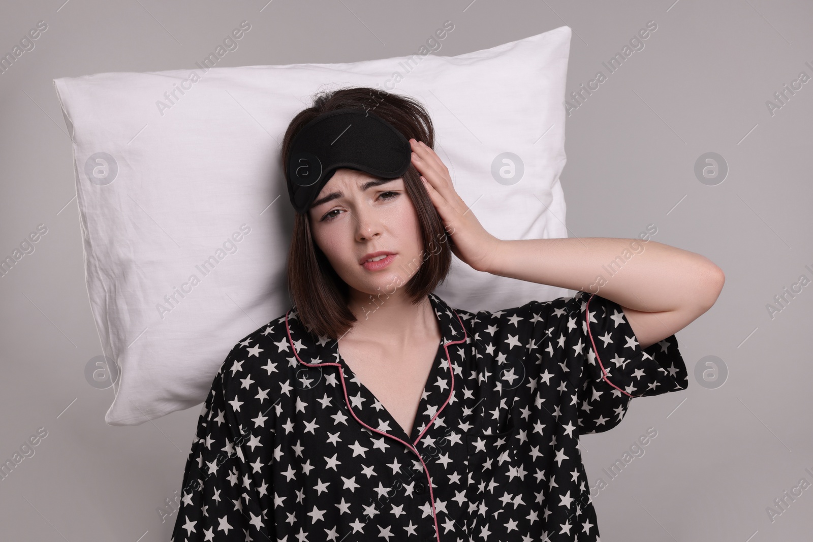 Photo of Tired young woman with sleep mask and pillow on light grey background. Insomnia problem