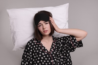 Tired young woman with sleep mask and pillow on light grey background. Insomnia problem