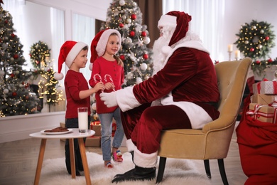 Photo of Santa Claus giving candy canes to children in room decorated for Christmas