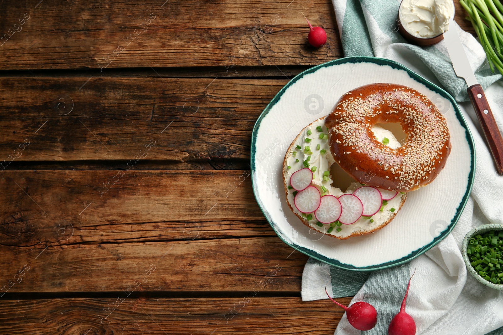 Photo of Delicious bagel with cream cheese, green onion and radish on wooden table, flat lay. Space for text