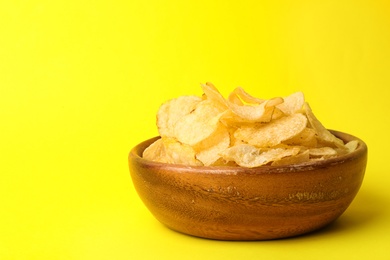 Delicious crispy potato chips in bowl on color background, space for text