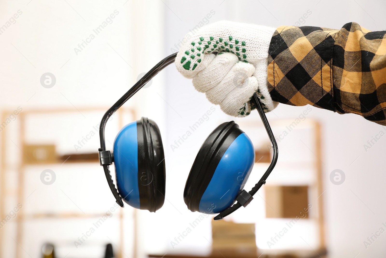 Photo of Worker holding safety headphones indoors, closeup. Hearing protection device