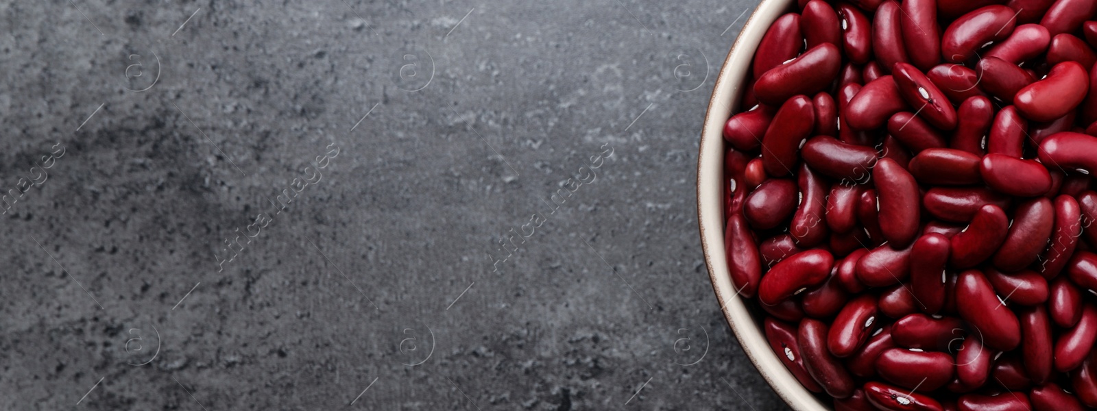 Image of Red kidney beans in bowl and space for text on grey table, top view. Banner design
