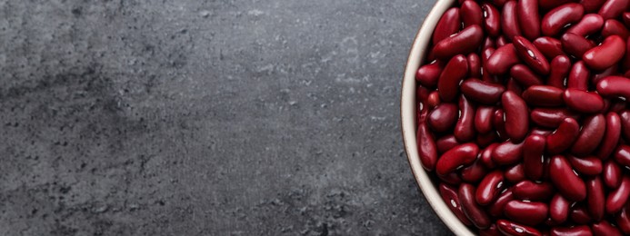 Red kidney beans in bowl and space for text on grey table, top view. Banner design