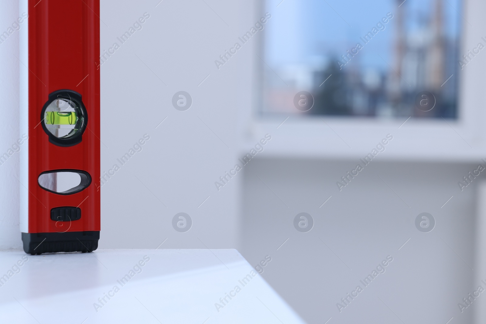 Photo of Red building level on white shelf indoors, closeup. Space for text