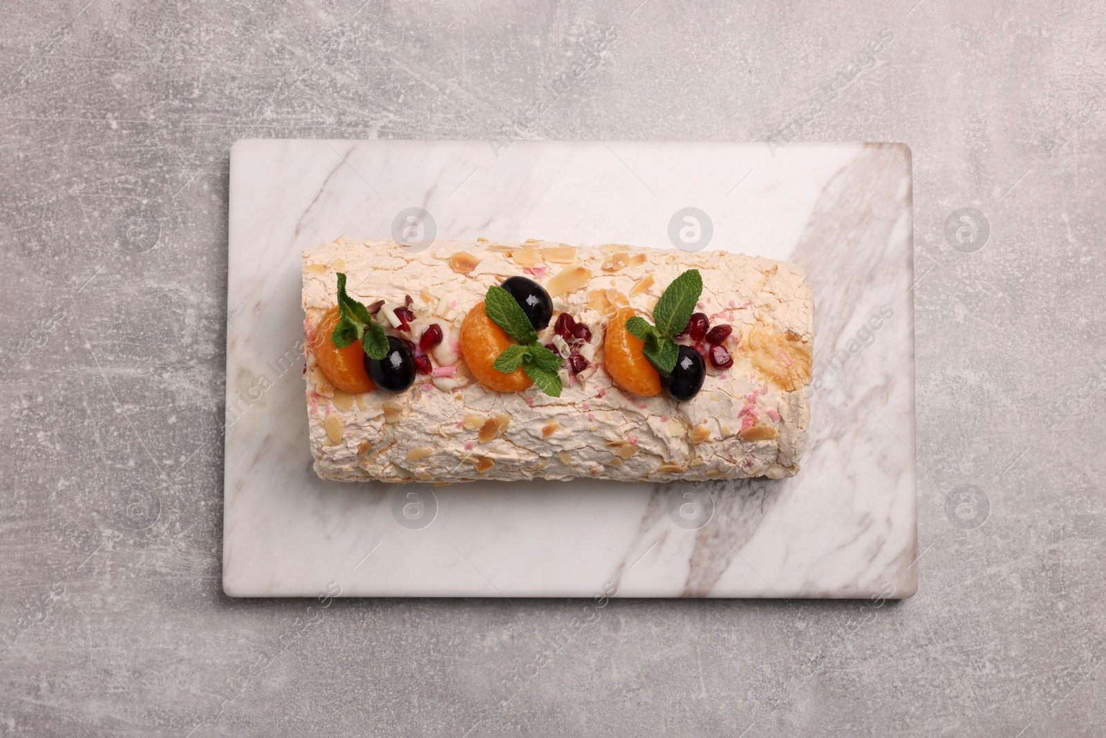 Photo of Tasty meringue roll with tangerine slices and mint leaves on grey table, top view