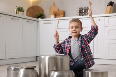 Photo of Little boy pretending to play drums on pots in kitchen