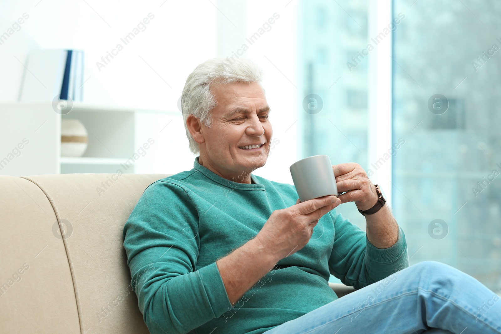 Photo of Portrait of mature man with cup of drink on sofa indoors