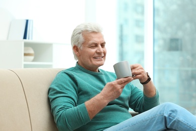 Portrait of mature man with cup of drink on sofa indoors