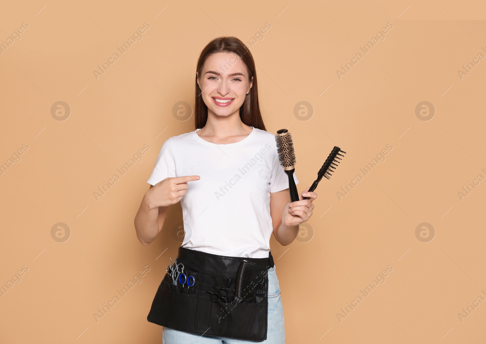 Photo of Portrait of happy hairdresser with brushes on beige background