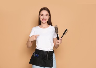 Portrait of happy hairdresser with brushes on beige background