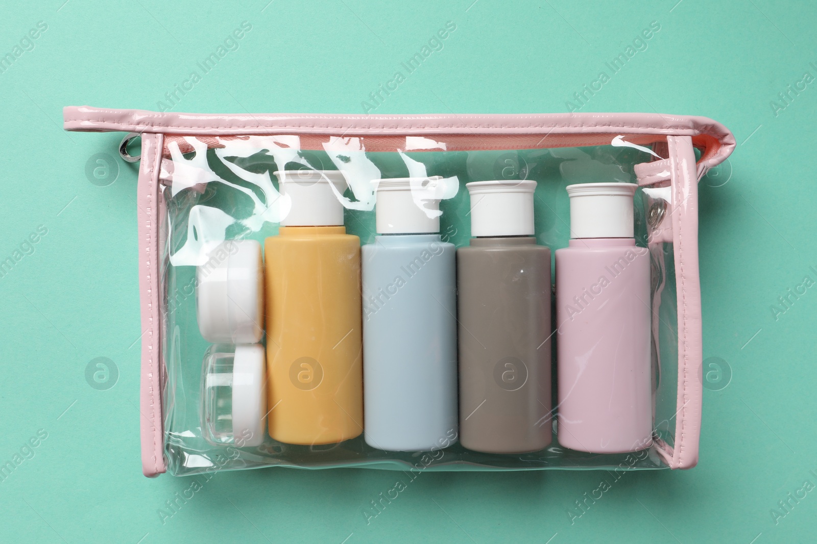 Photo of Cosmetic travel kit in plastic bag on turquoise background, top view. Bath accessories