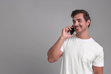 Photo of Handsome young man talking on smartphone against grey background. Space for text