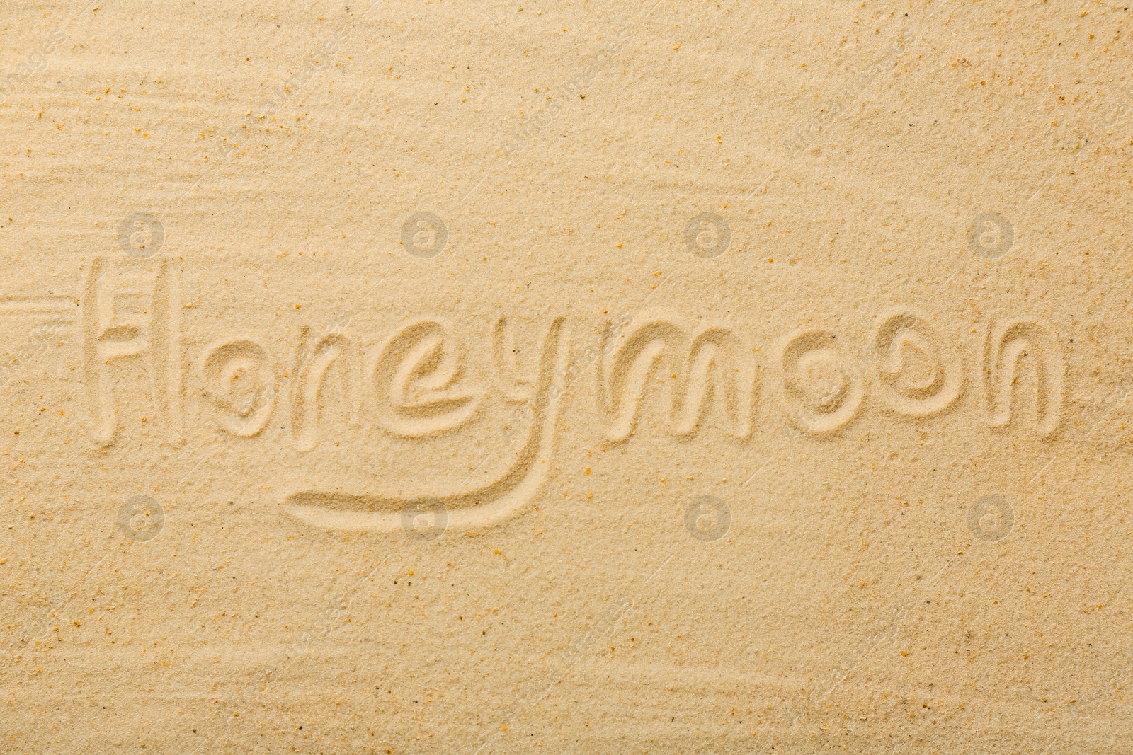 Photo of Word Honeymoon written on sand, top view
