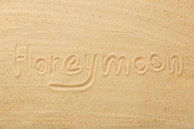 Photo of Word Honeymoon written on sand, top view