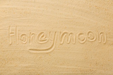 Word Honeymoon written on sand, top view