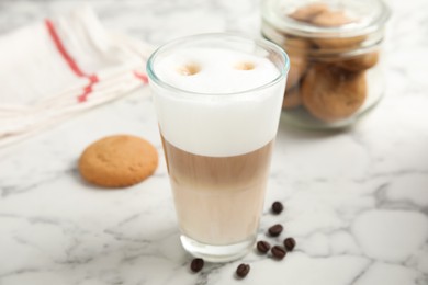 Delicious latte macchiato, cookies and coffee beans on white marble table