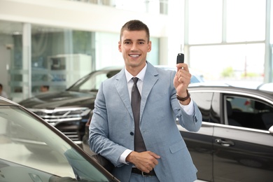 Young salesman with key near car in modern dealership