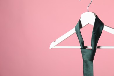 Photo of Hanger with teal tie on pink background, closeup. Space for text