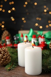 Burning candles and festive decor on wooden table against blurred Christmas lights