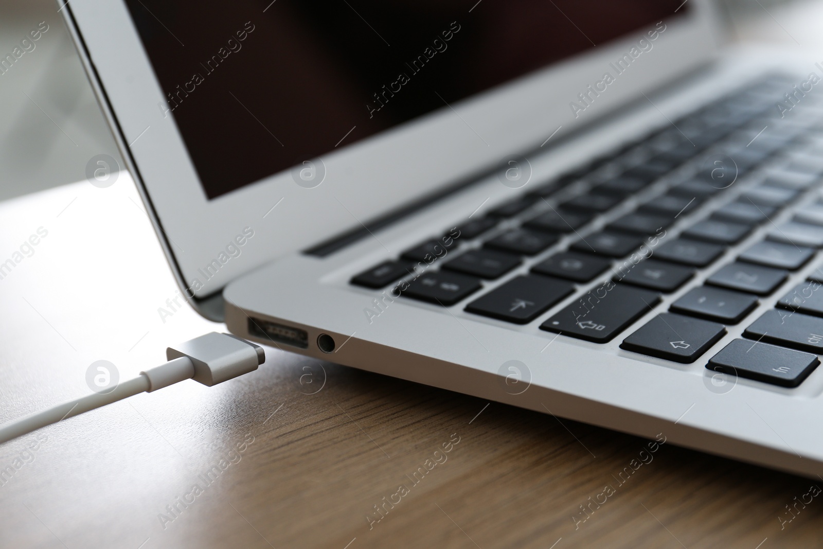 Photo of Modern laptop and charging cable on wooden table, closeup