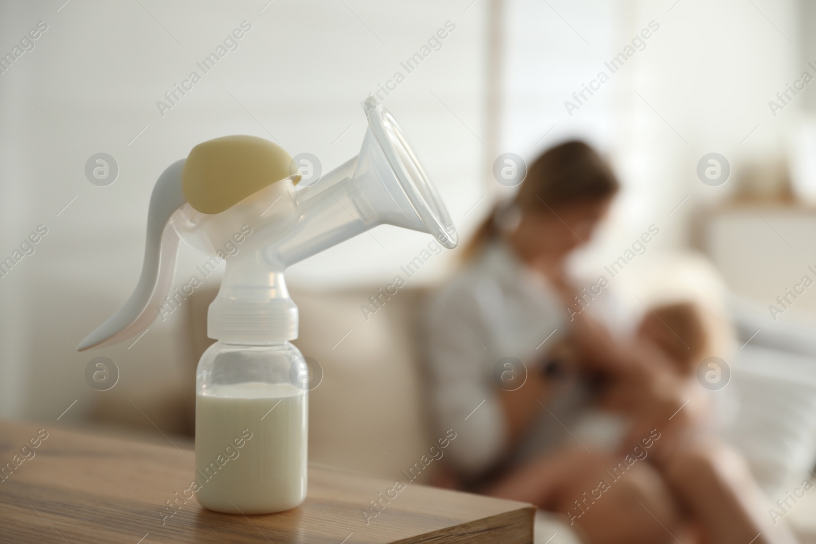 Photo of Mother feeding her little baby at home, focus on breast pump with milk. Healthy growth